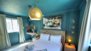 A neatly made bed with towels, a hanging light fixture, a wall-mounted picture, and a bedside table with a lamp.