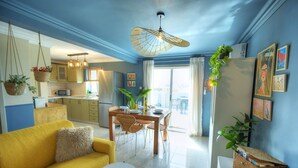 A modern kitchen with hanging baskets, a dining area with a table and chairs, and a yellow sofa.