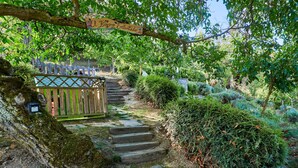 Een houten trap die leidt naar een poort met een bord, omgeven door groen en een hek.