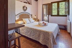 Un dormitorio con cama, suelo de madera, una mesita de noche, una ventana con contraventanas y una estantería en la pared.