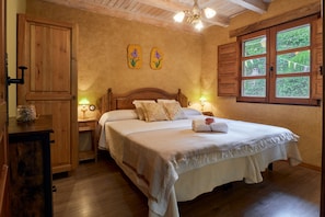 A bedroom with a wooden bed, two wall-mounted lamps, a window with shutters, and a wooden wardrobe.
