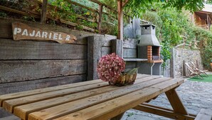 Un banco de madera con un jarrón de hortensia rosa, un muro de piedra y un cartel que dice 'PAJARIEL 2'.