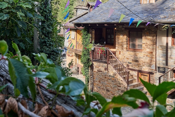 A stone building with a wooden staircase, ivy, and colorful triangular flags.