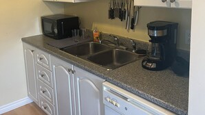 A kitchen with white cabinetry, a granite countertop, a dishwasher, a coffee maker, and a microwave.