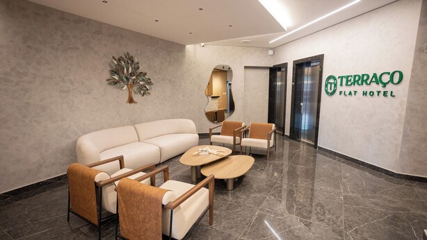 Un vestíbulo moderno con sofá, sillones y una mesa de centro. Una decoración arbórea adorna la pared, y se observa el letrero del Terraço Flat Hotel.