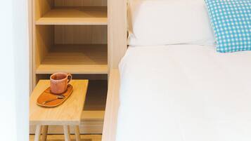 Habitación de hotel con cama, una mesita con taza y platillo, almohada de cuadros y un estante de madera con un cuadro enmarcado.