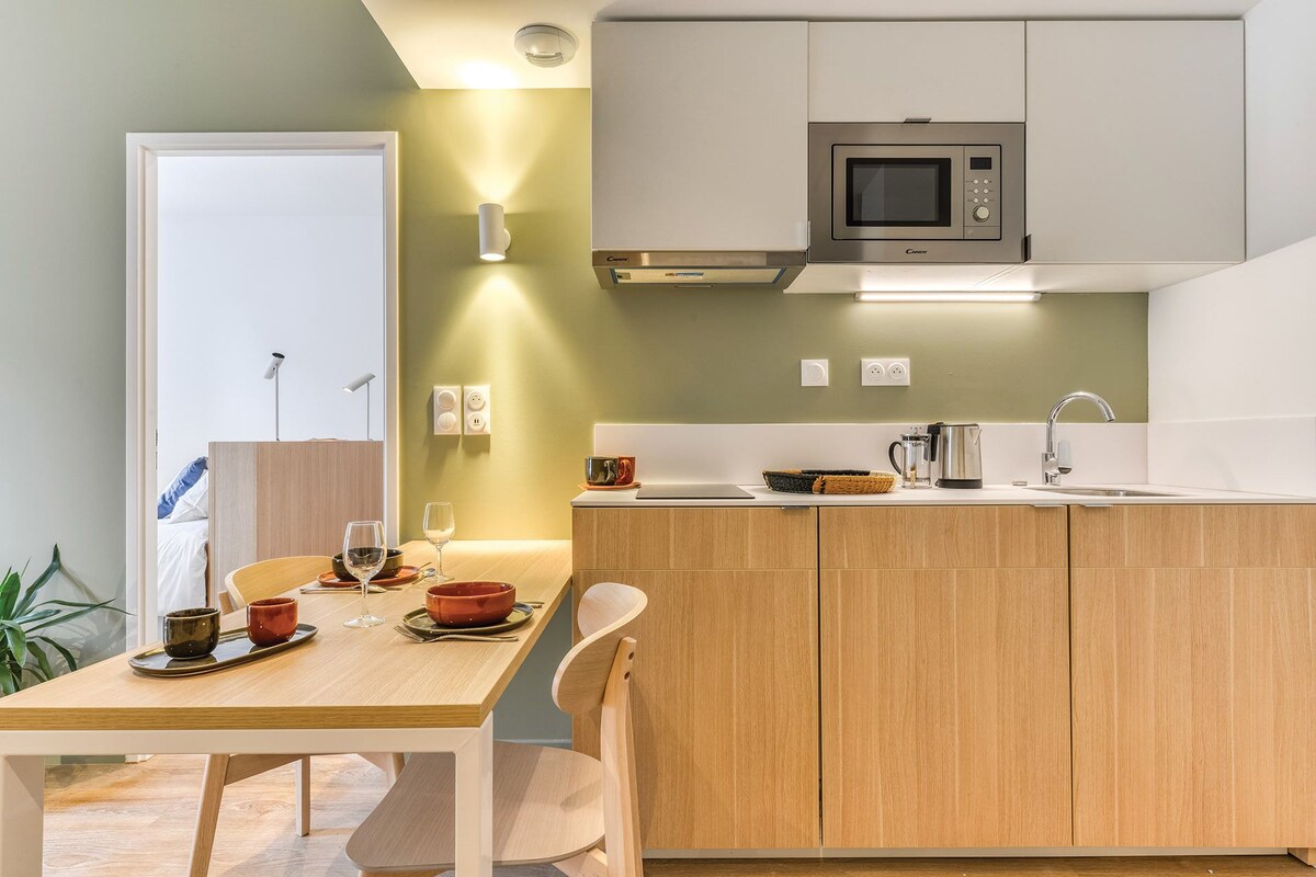 A modern kitchen with wooden cabinets, a built-in microwave, and a dining area with a table set for two.