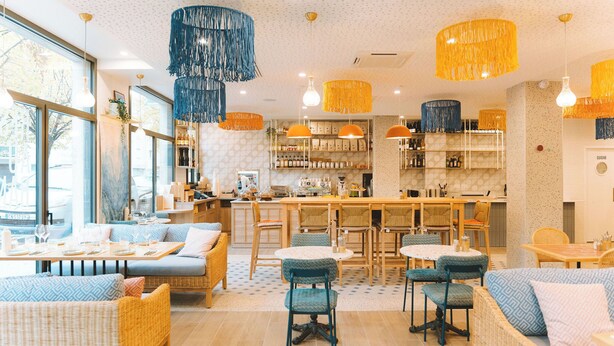 Ein modernes Restaurant mit Korbm öbeln, hängenden Pendelleuchten und einem im Hintergrund sichtbaren Küchenbereich.
