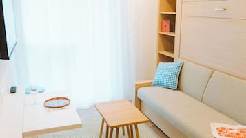 Una sala de estar moderna con un sofá, una mesita, un televisor montado en la pared y un mueble de madera con estantes.