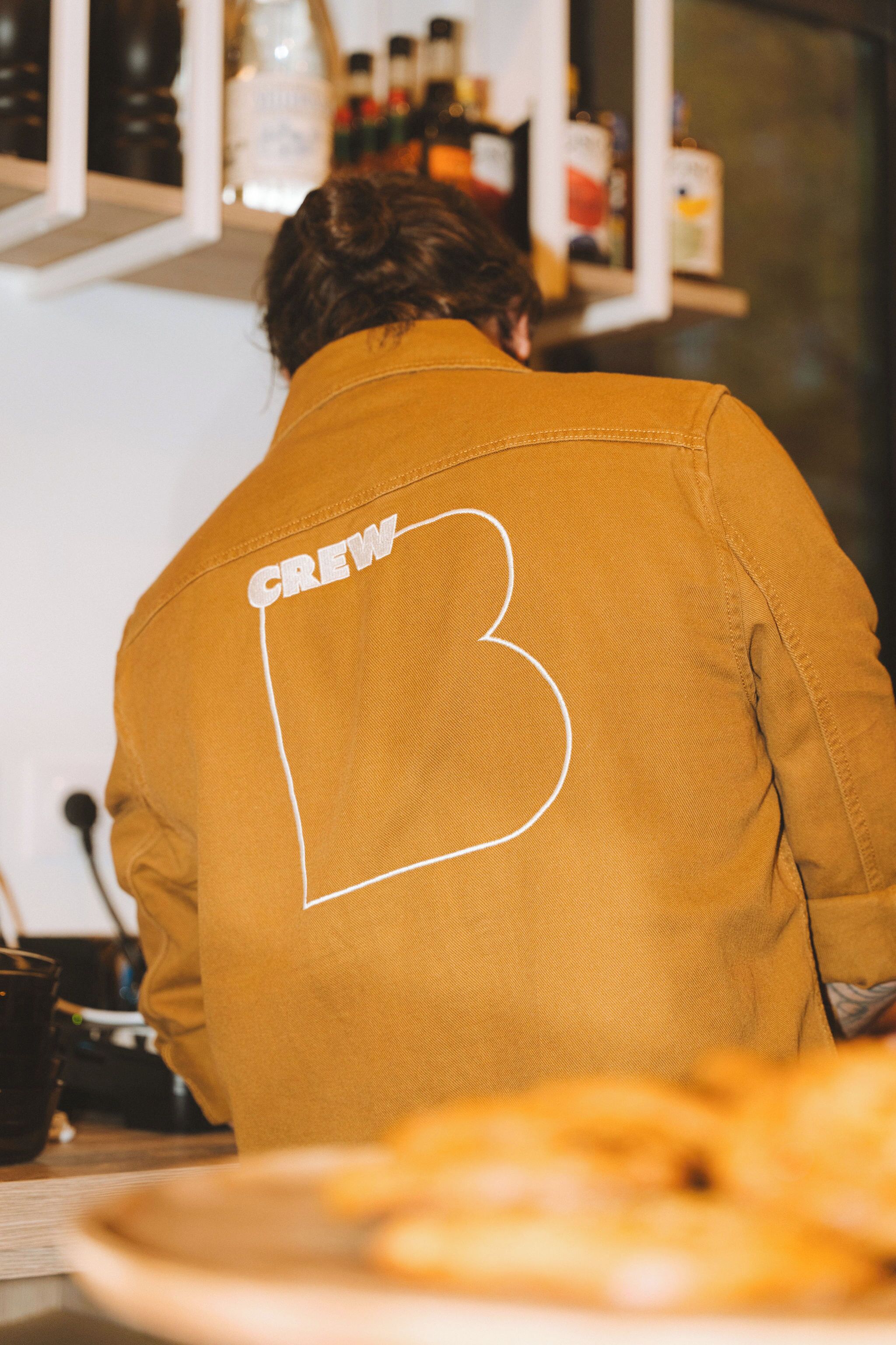 Una persona con una chaqueta que lleva la palabra 'CREW' y una gran letra 'B' en la espalda.