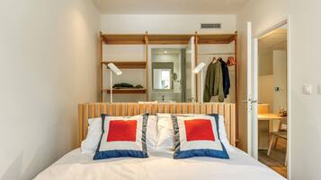 Una camera da letto con un letto, una testiera in legno, un armadio con abiti appesi e uno specchio.
