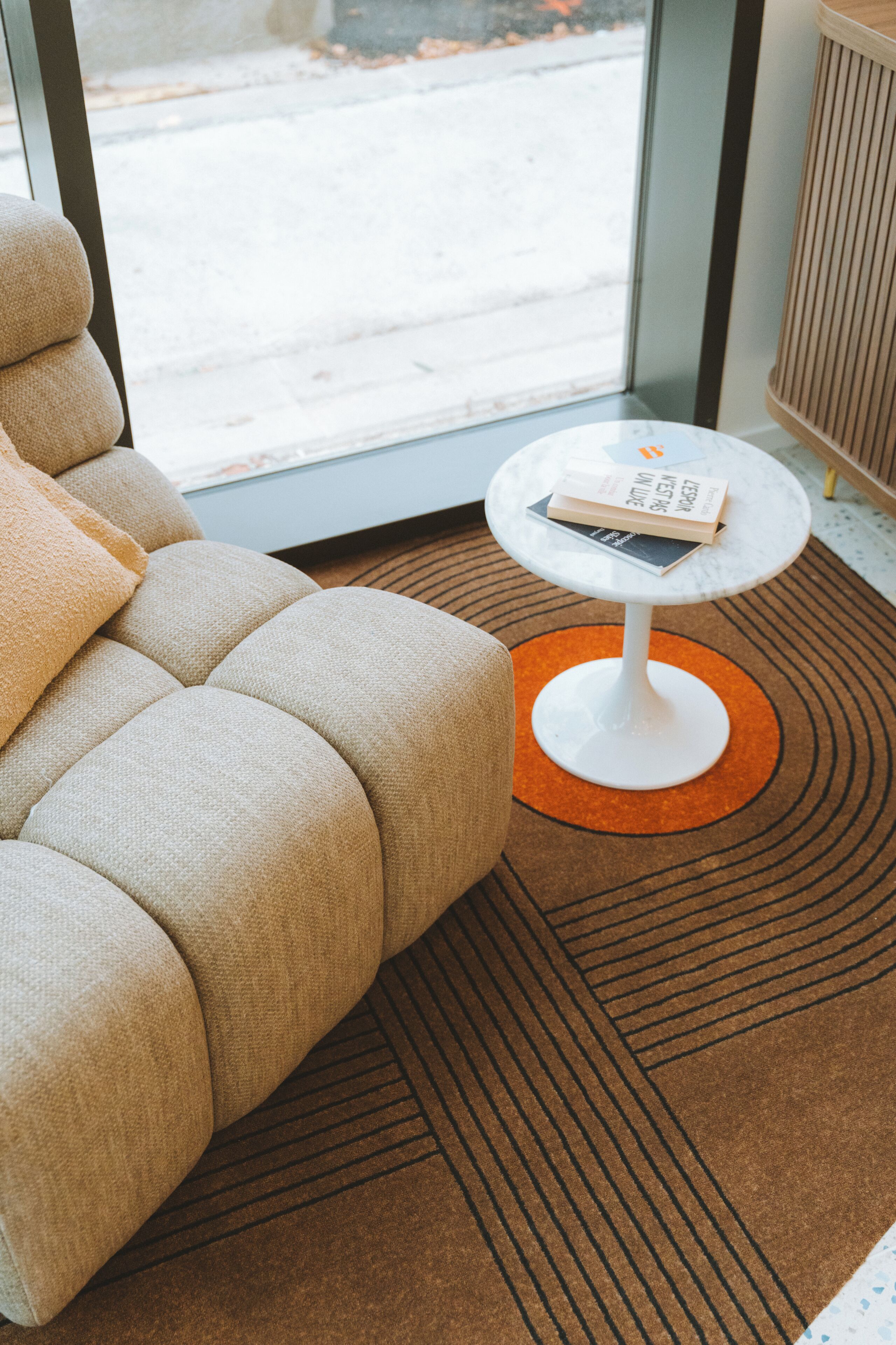Une pièce moderne avec un canapé, une petite table blanche sur laquelle se trouve un livre, et un tapis à motifs.
