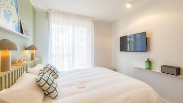 Habitación de hotel con una cama, televisión montada en la pared, teléfono y lámpara en una mesita de noche.