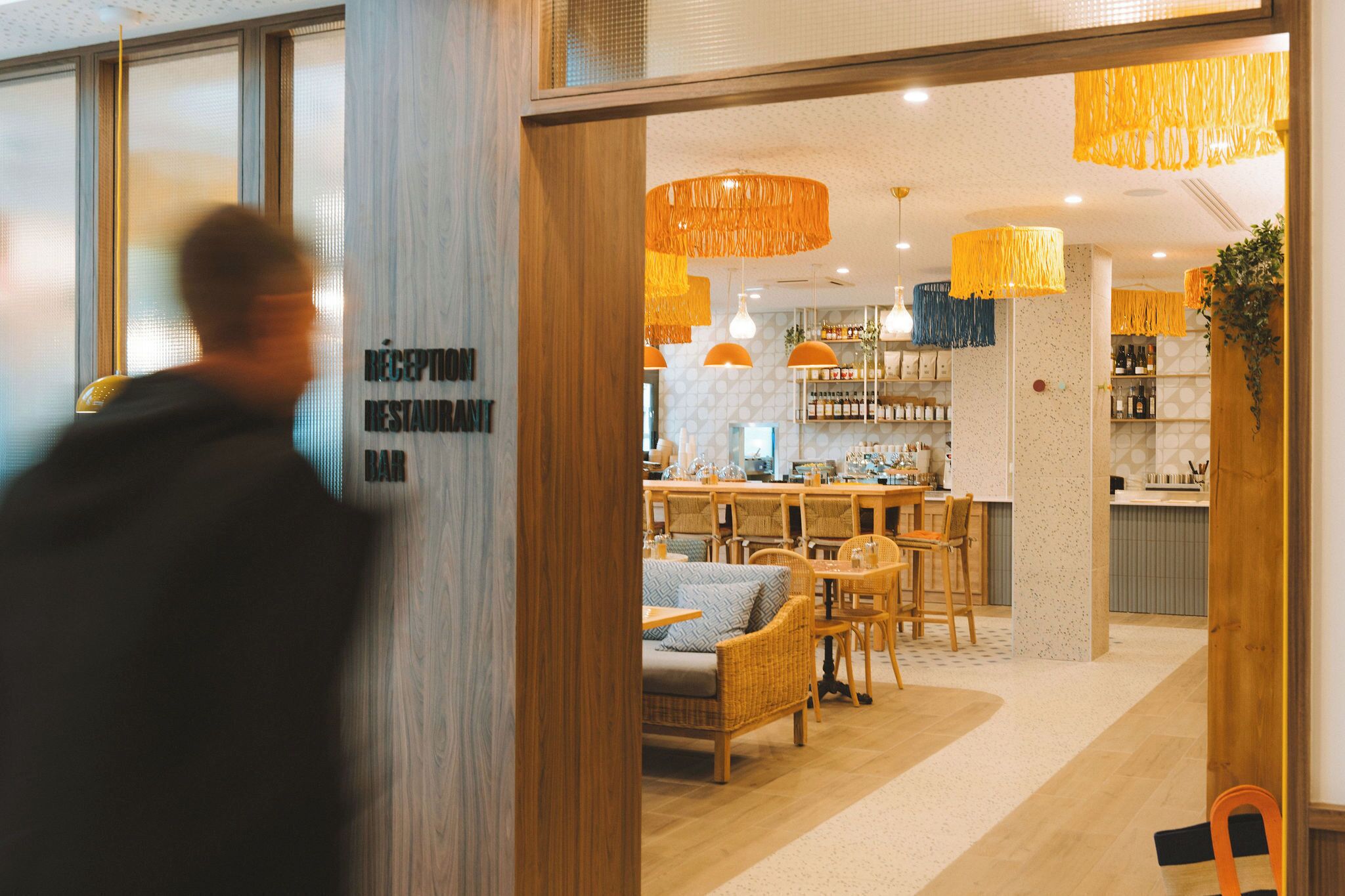 En restaurantindretning med træmøbler, hængende orange lamper og et barområde.