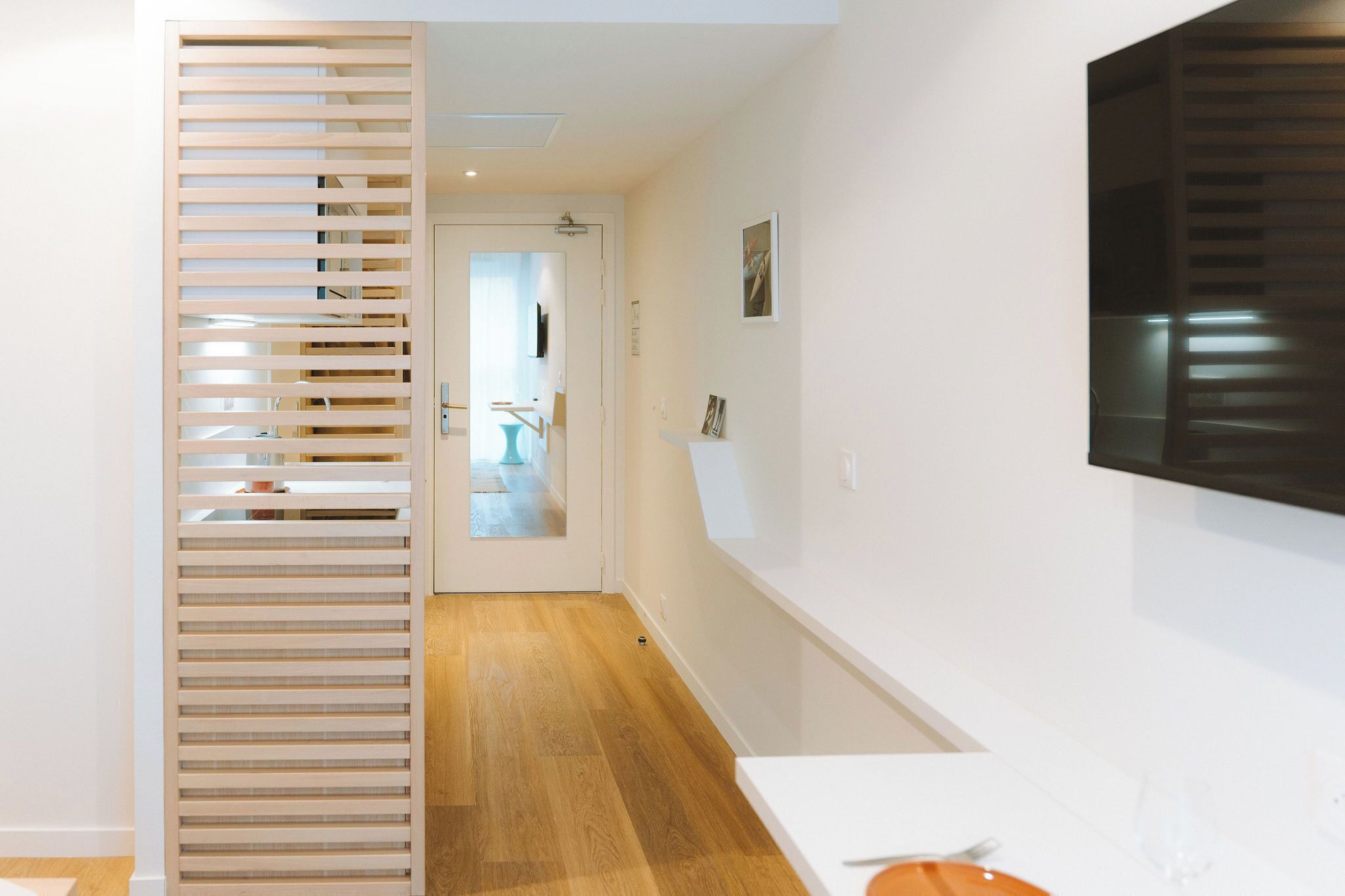 Un intérieur moderne avec une cloison en lattes de bois, un téléviseur blanc fixé au mur et un plancher en bois.