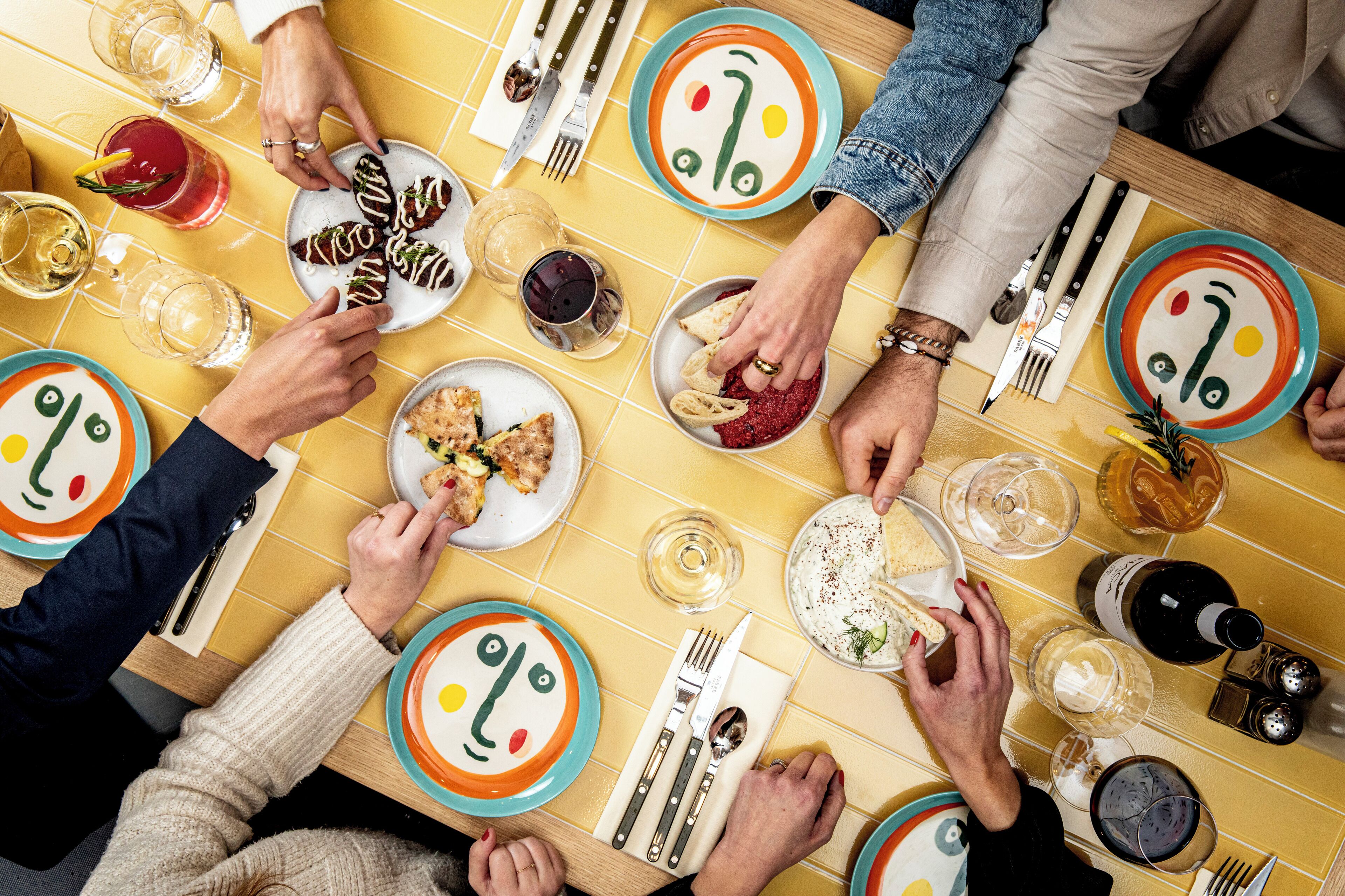 Un grupo de personas cenando en una mesa con platos, cubiertos y vasos.