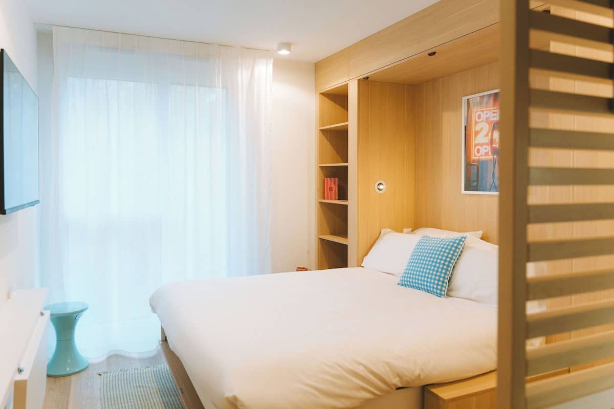 Un dormitorio con cama, mesita de noche, armario y ventana con cortinas.