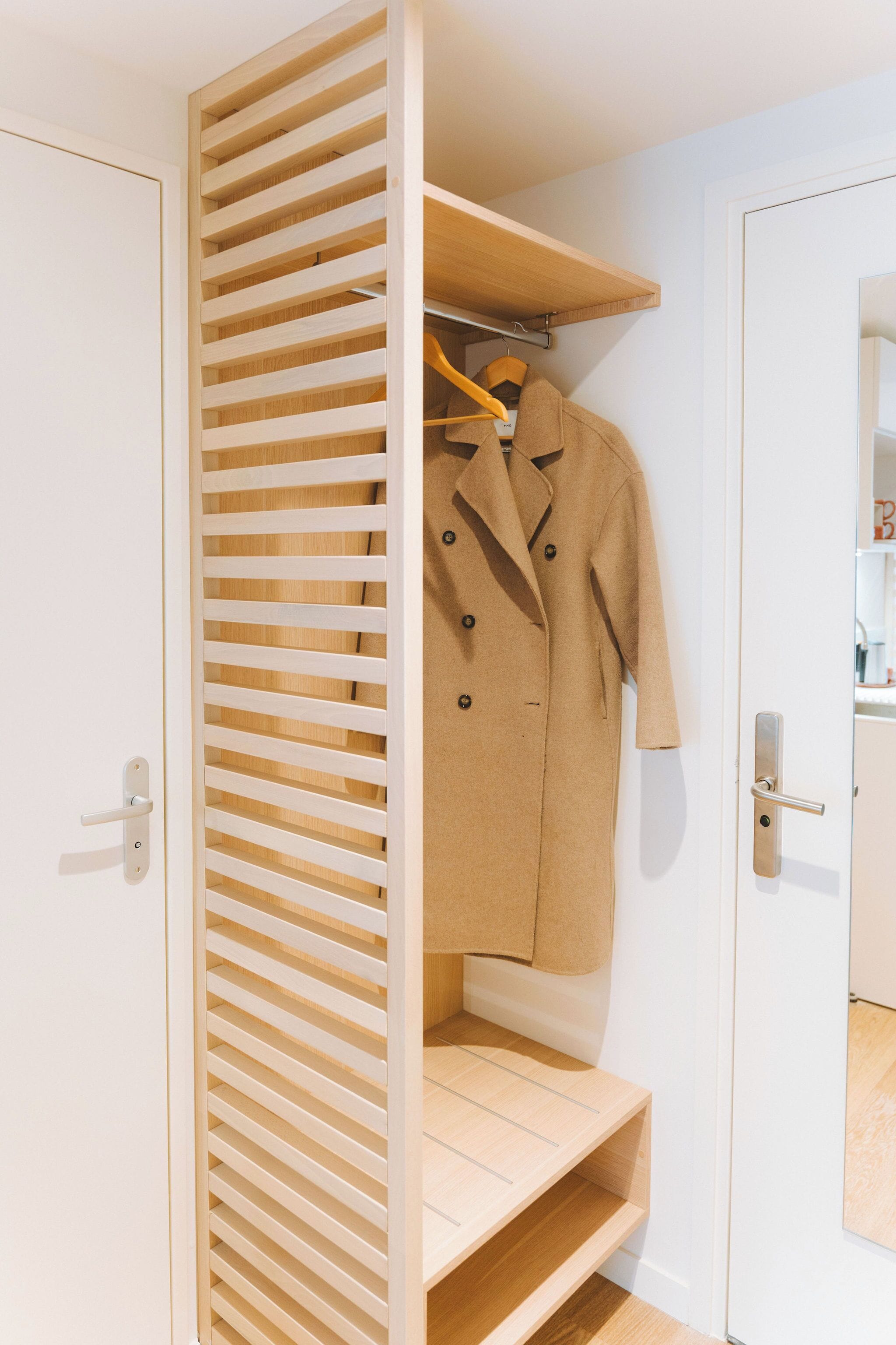 Un dressing ouvert avec un motif de lattes en bois, un manteau suspendu à un cintre et une poignée de porte visible.