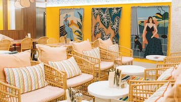 Un espacio lounge vibrante con muebles de mimbre, alfombras a rayas de colores y murales artísticos en las paredes.