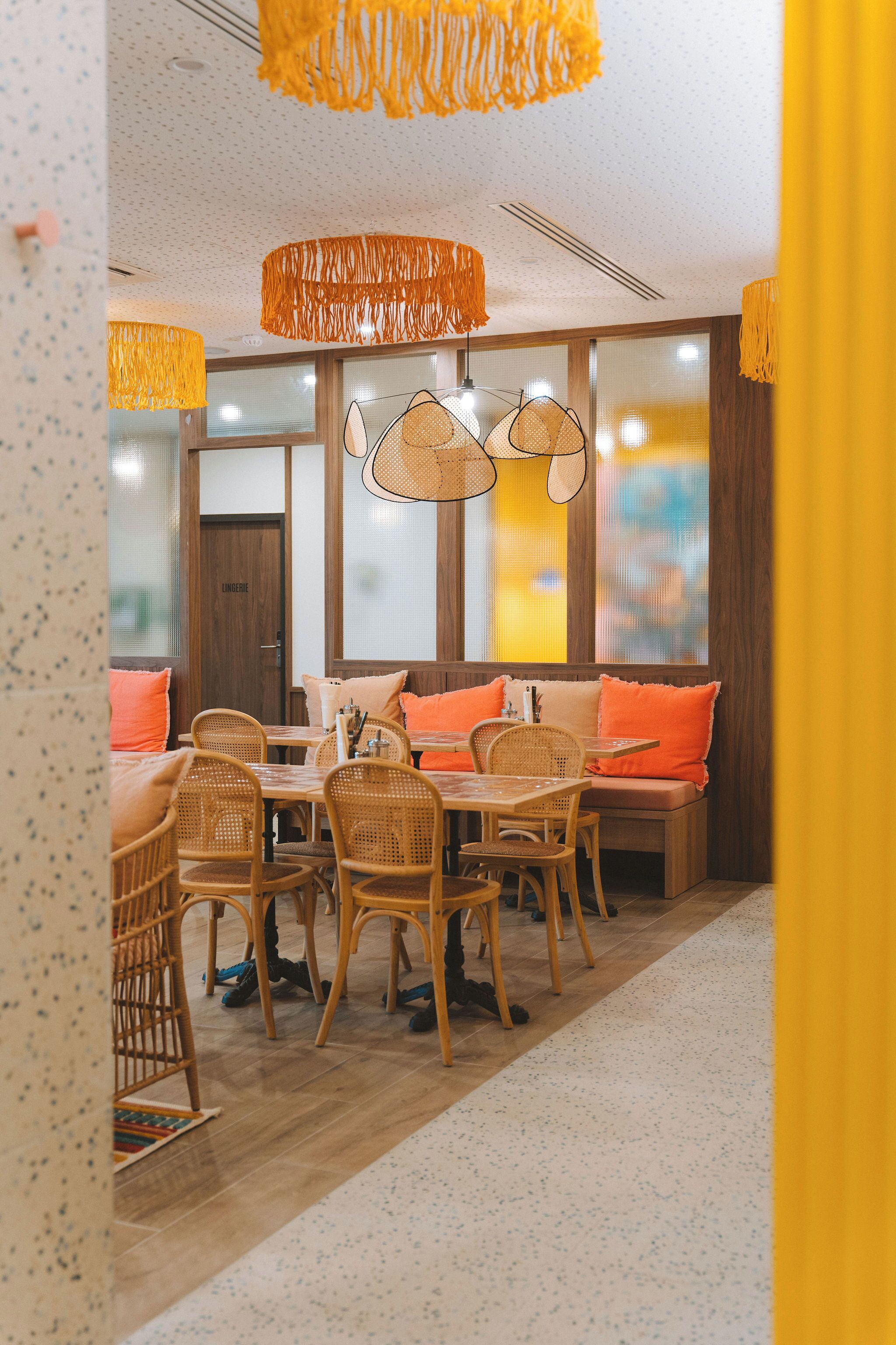 A dining area with wicker furniture, orange cushions, and hanging pendant lights.
