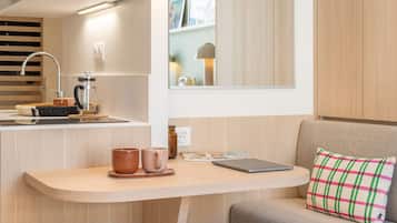A compact kitchenette with a sink, coffee maker, and a small table with two mugs and a laptop.