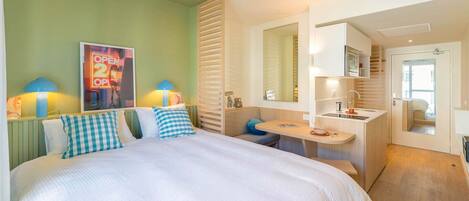 A hotel room with a bed, a desk, a mirror, and a small kitchenette.