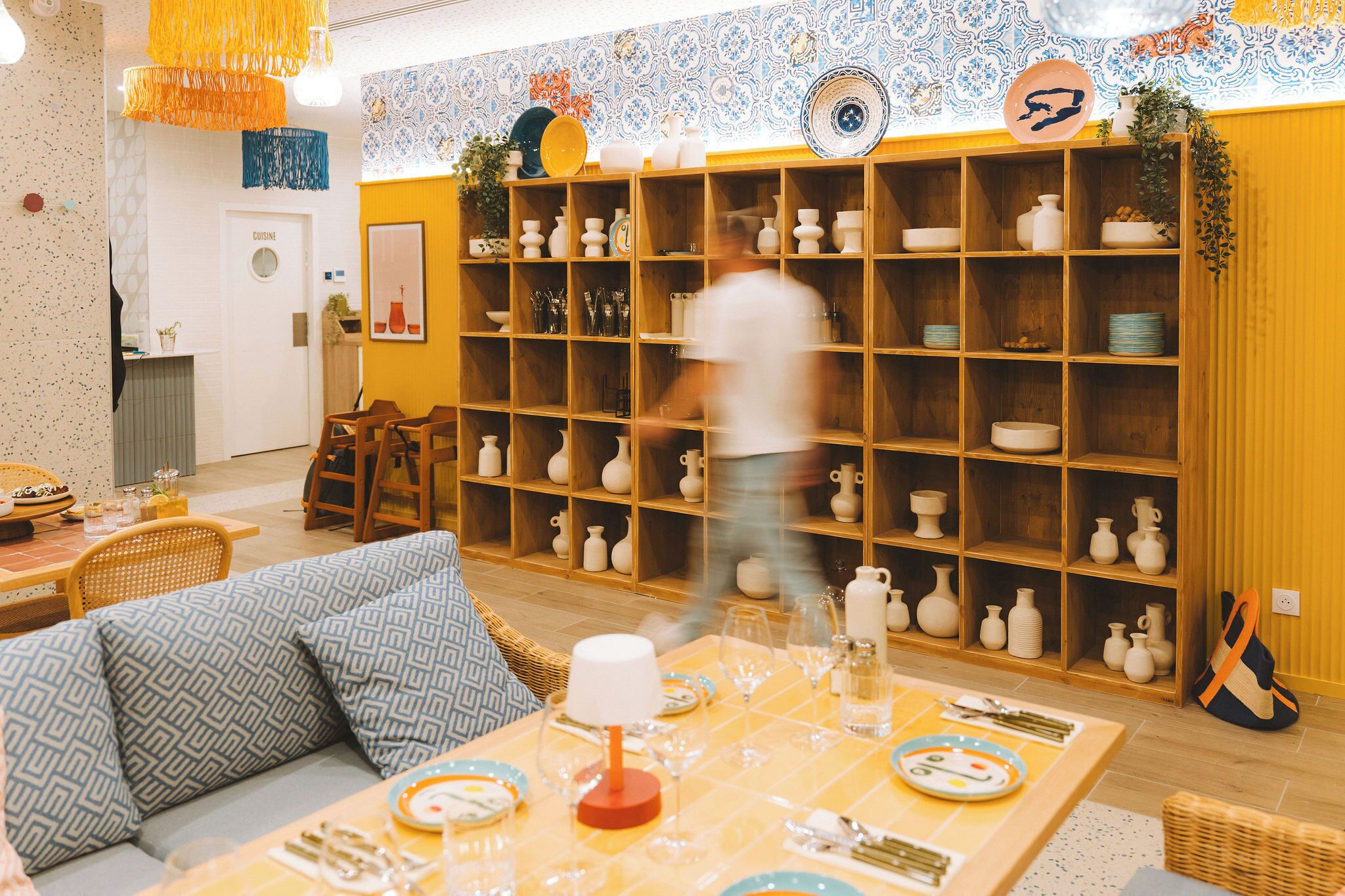 A dining area with a wooden table set for a meal, surrounded by shelves of white pottery.