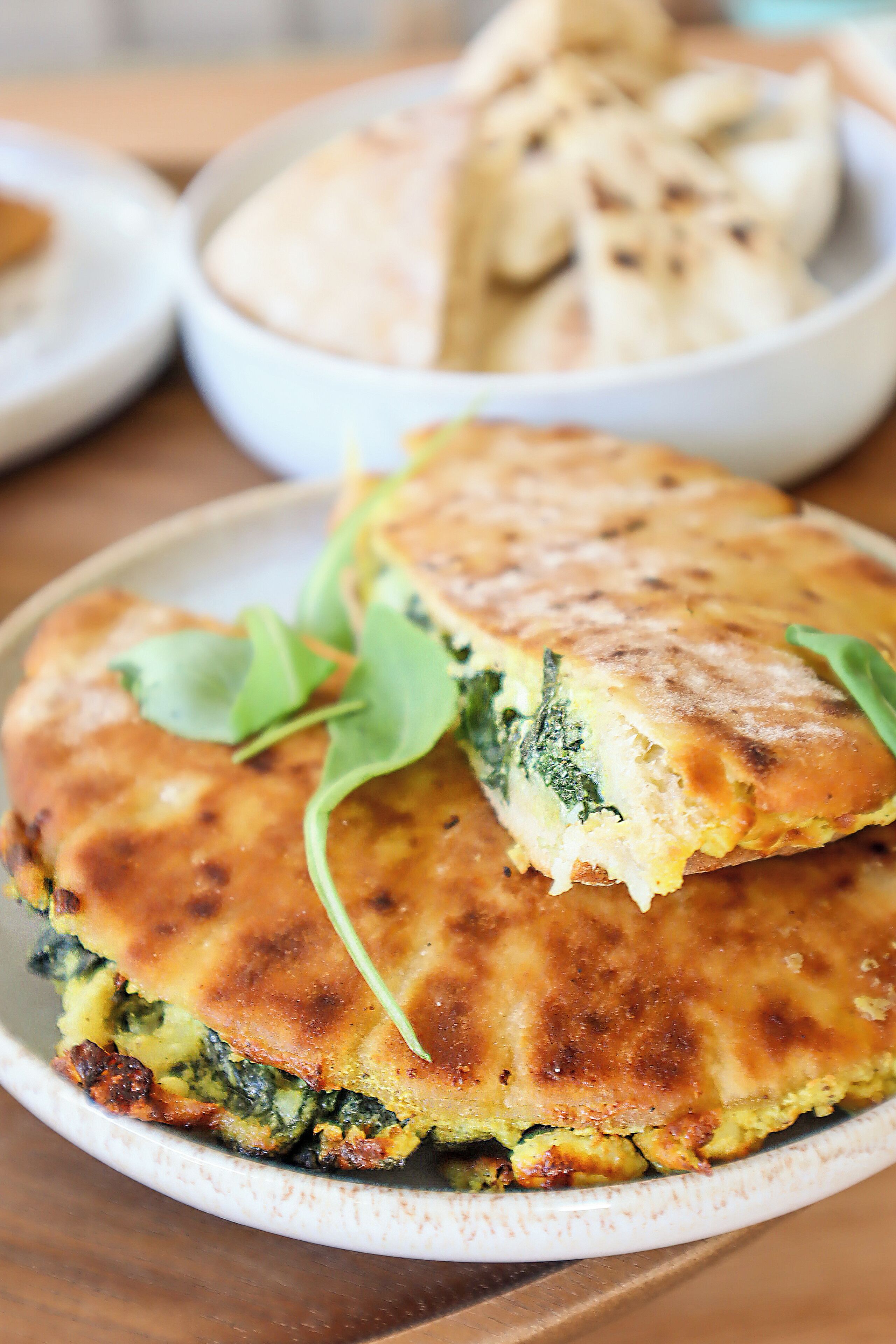 A plate with a food item, possibly a flatbread or pastry, with a golden-brown crust and green leafy garnish.