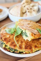 Un piatto con un alimento, forse una focaccia o un dolce, con una crosta dorata e guarnizione di foglie verdi.