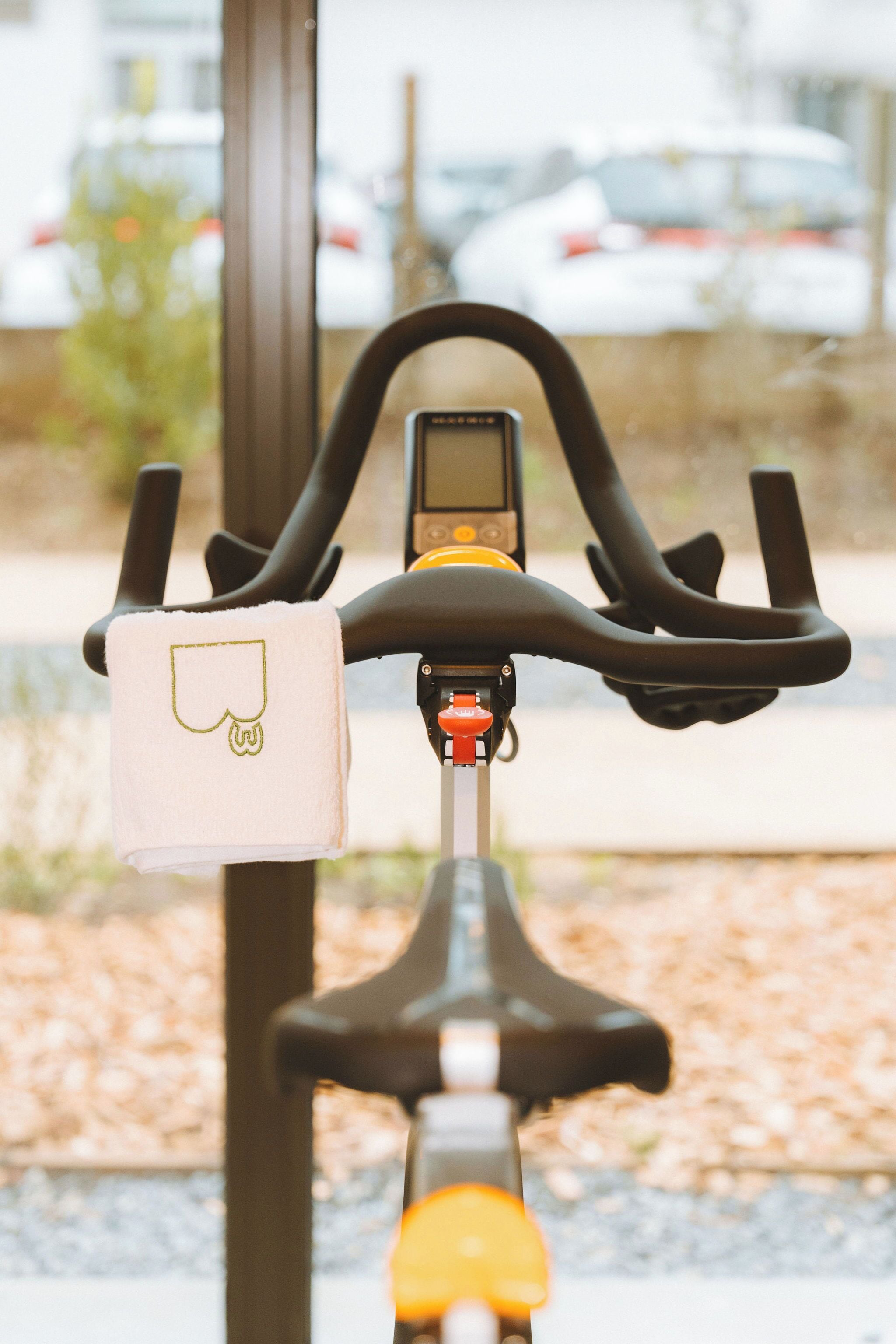Ein stehendes Fitnessrad mit Digitalanzeige und einem Handtuch, das an der Lenkstange hängt.
