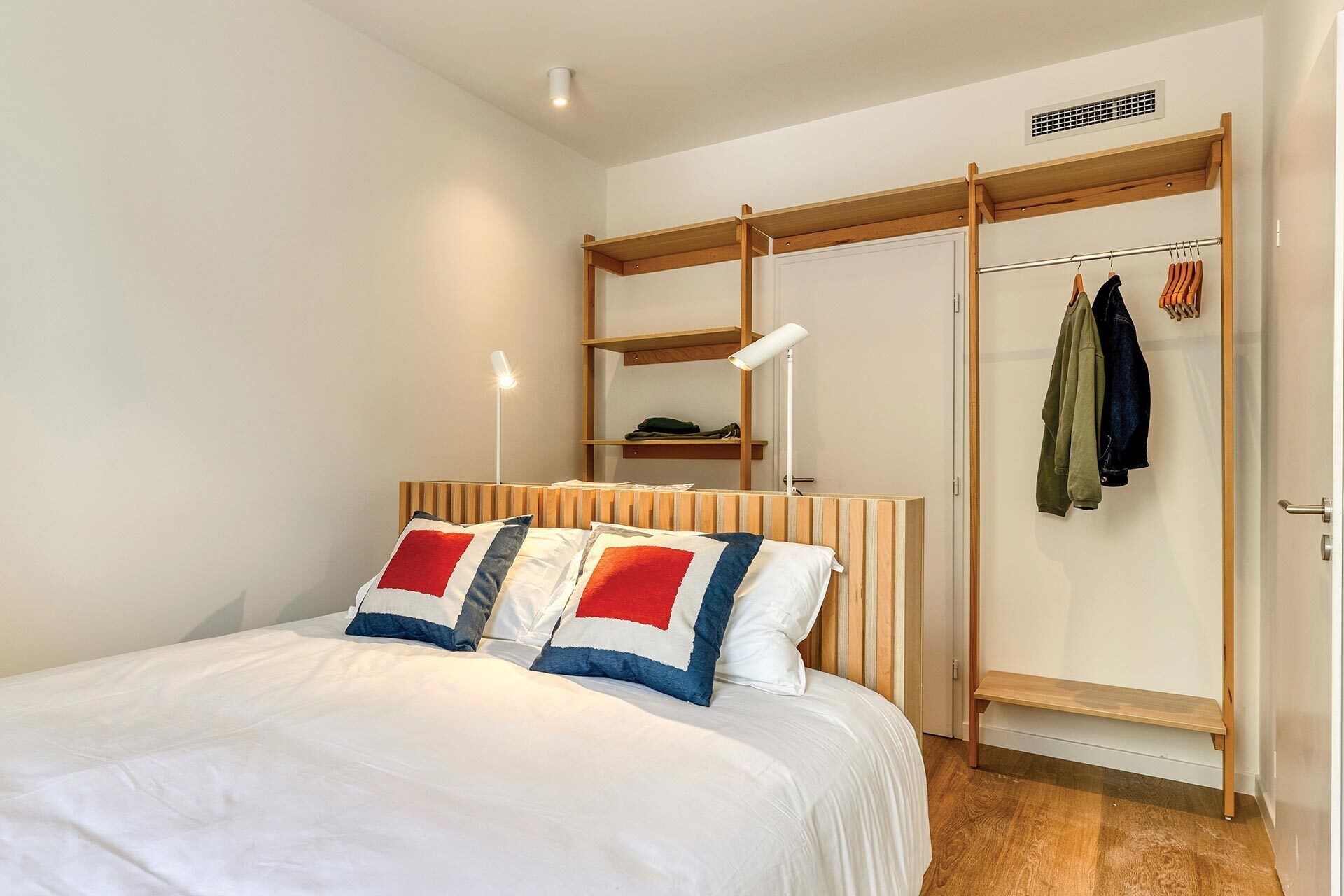 A bedroom with a bed, a wooden headboard, a wardrobe with a mirror, and a hanging clothes rack.