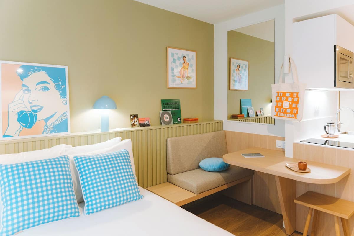 Une chambre d’hôtel compacte comprenant un lit, un canapé, un petit coin cuisine et une table à manger.