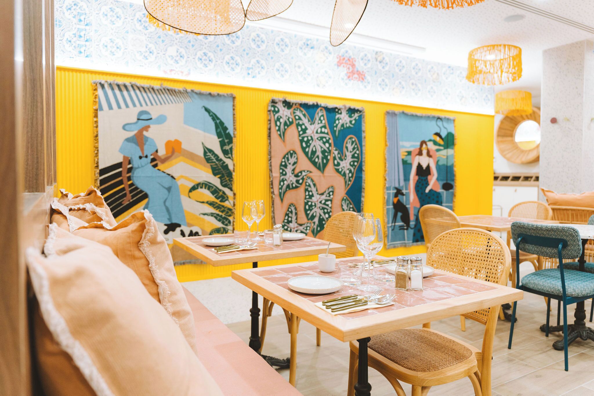 Un restaurante con mesas y sillas de madera, paredes amarillas y coloridas obras de arte en las paredes.