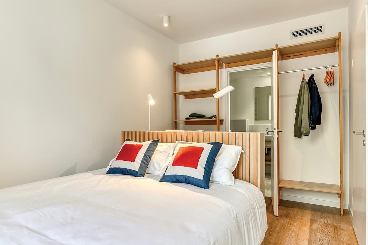 Un dormitorio con cama, armario, espejo y perchero.