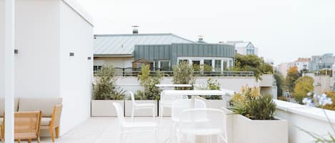 A rooftop terrace with white chairs and tables, a white sofa, and potted plants.