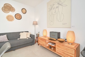 Ett vardagsrum med en grå soffa, ett sidobord i trä, konst på väggen och en lampa.