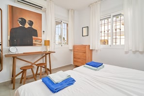 Ett hotellrum med två sängar, ett skrivbord, en stol, en byr å i trä och en tavla på väggen.