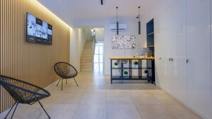 A modern hallway with a wooden slat wall, a black chair, a blue console table with plants, and a staircase in the background. - Rooftop Parthenopeo - Contemporary Rooms (Naples)