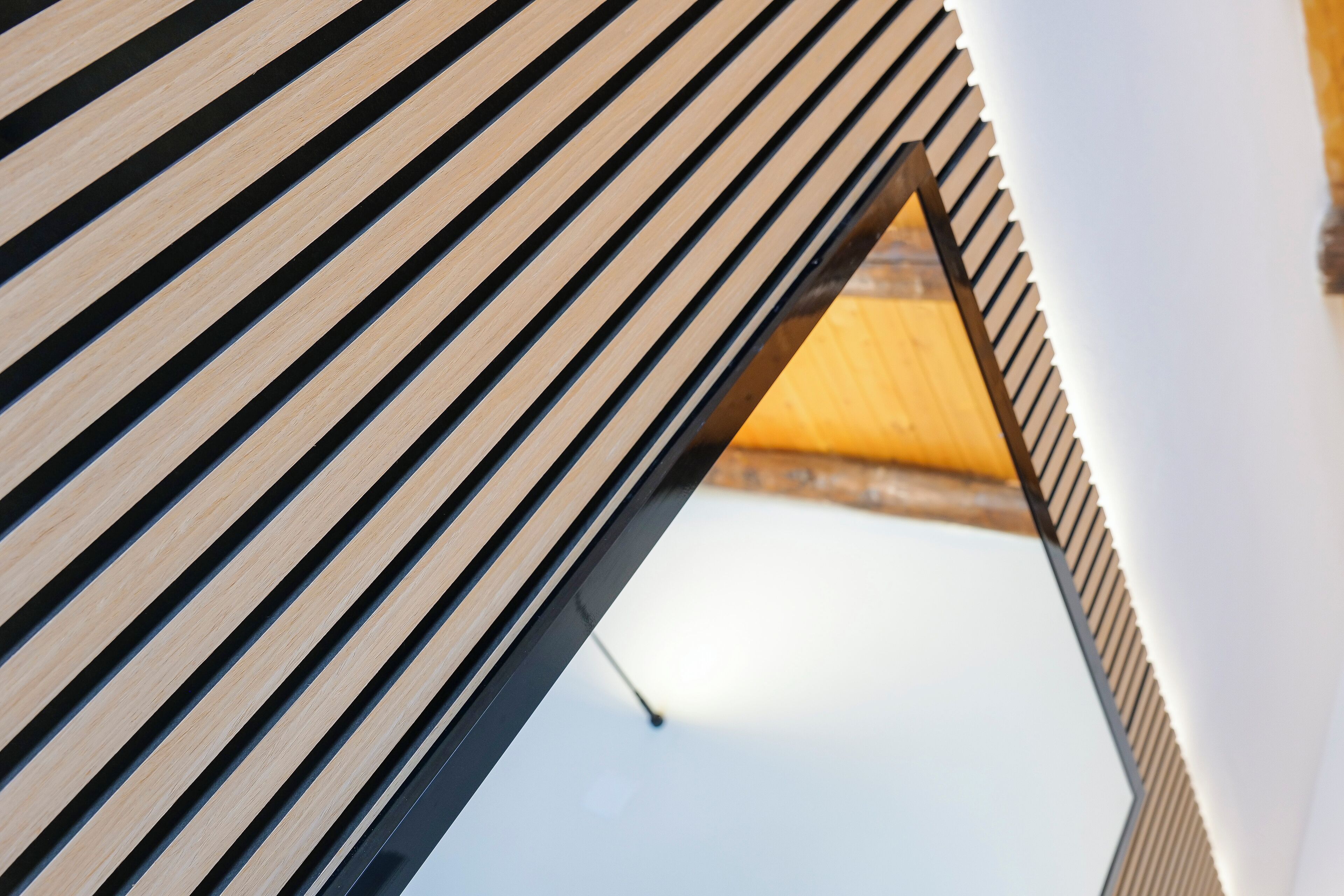A close-up of a wooden slatted ceiling with a triangular cutout revealing a wooden interior.