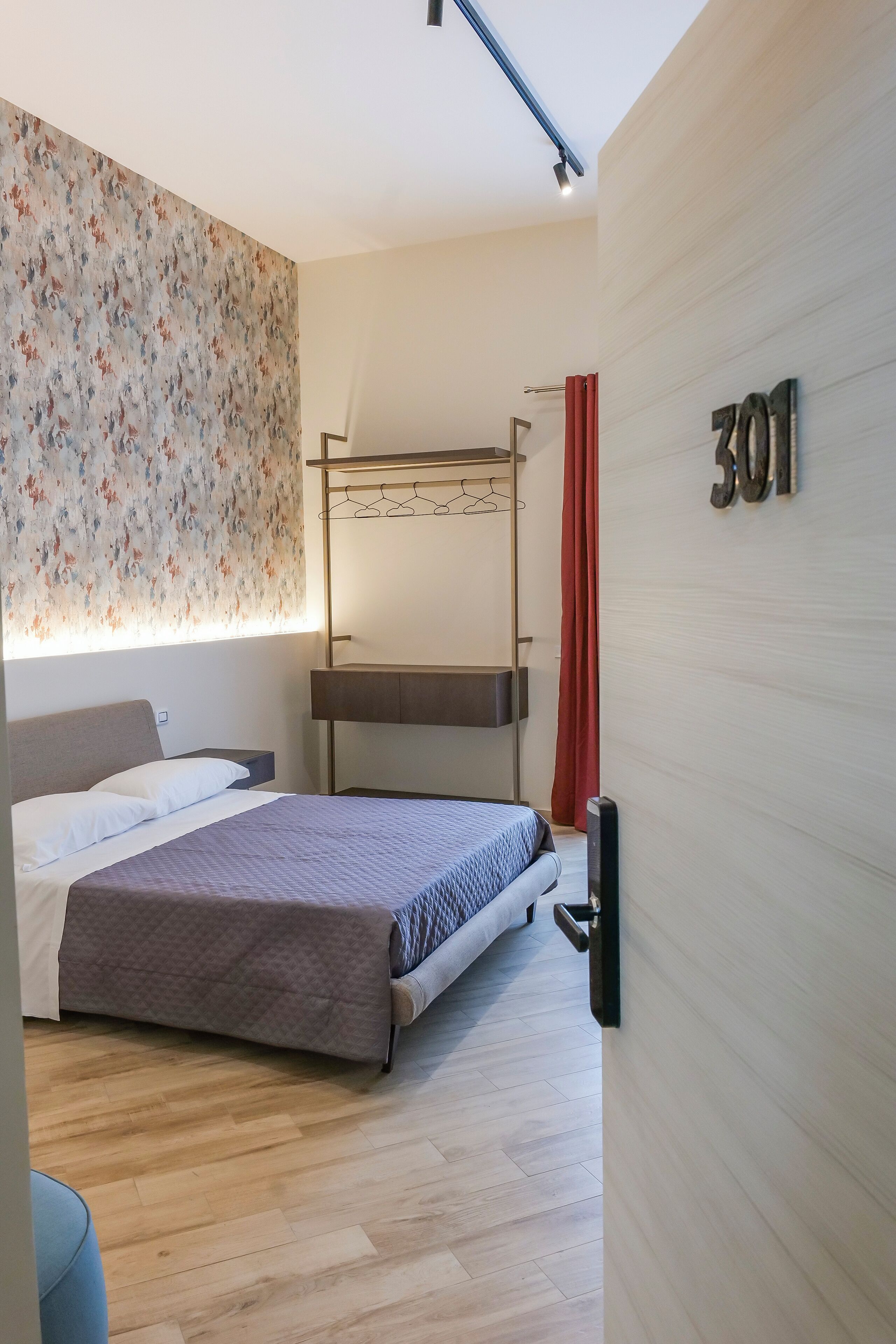 Ett modernt hotellrum med en våningssäng, ett sängbord, en väggmonterad TV och en nummerskylt som visar rummets nummer.