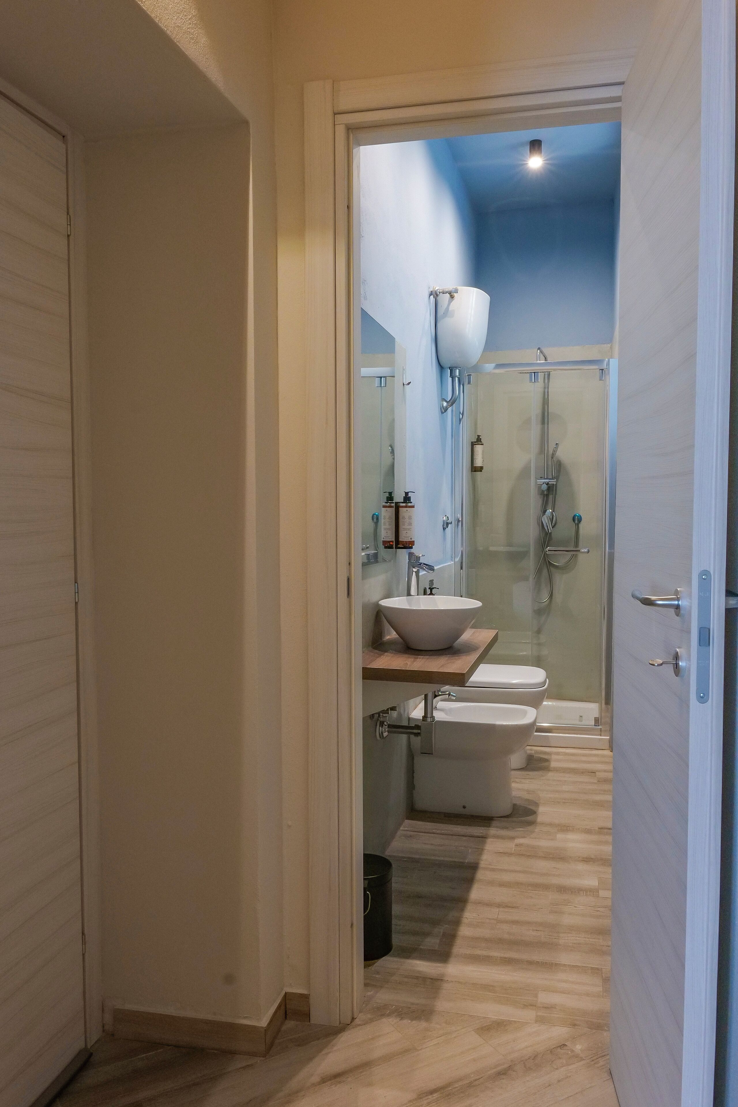 A modern bathroom with a wooden vanity, a large mirror, a white sink, two toilets, and a glass-enclosed shower area.