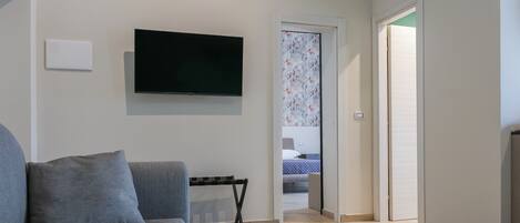 Una sala de estar moderna con un sofá gris, un televisor de pantalla plana montado y piso de madera.