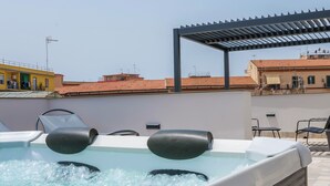 A hot tub with two black seats, a pergola, and a view of buildings in the background. - Rooftop Parthenopeo - Contemporary Rooms (Naples)