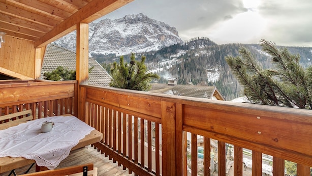 A wooden balcony with a table, a chair, and a view of snow-capped mountains.