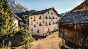 A traditional building with multiple windows and flower boxes, a wooden structure to the right, and a mountain in the background.