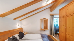 A bedroom with a wooden ceiling, a bed with pillows, a nightstand, a mirror, and wooden cabinets.