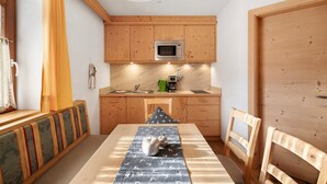 A compact kitchen with wooden cabinets, a microwave, and a dining area with a table and chairs. - Studio Apartment 'Apartment Ramei' with Mountain View, Shared Garden and Wi-Fi (La Valle)