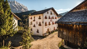 A traditional building with multiple windows and flower boxes, a wooden structure to the right, and a mountain in the background. - Studio Apartment 'Apartment Ramei' with Mountain View, Shared Garden and Wi-Fi (La Valle)