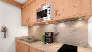 A kitchen with wooden cabinets, a built-in microwave, a coffee maker, and an induction cooktop. - Studio Apartment 'Apartment Ramei' with Mountain View, Shared Garden and Wi-Fi (La Valle)