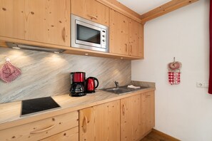 A kitchen with wooden cabinets, a microwave, a coffee maker, and a sink. - Studio Apartment 'Apartment Plaies' with Mountain View, Shared Garden and Wi-Fi (La Valle)